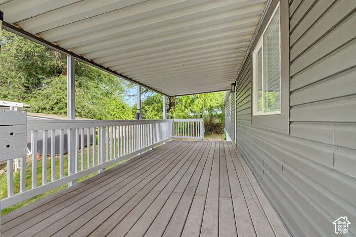 Covered outdoor deck with wood-finish flooring, white railing, and gray siding