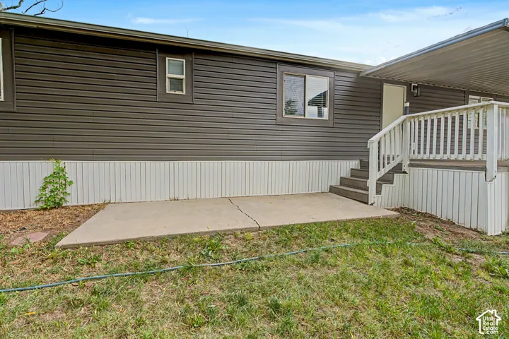 Gray horizontal siding with white vertical skirting, concrete patio, and a covered porch with white railings