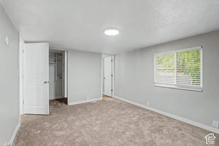 Neutral wall color, window with blinds, overhead flush mount lighting, carpeted flooring, and a closet with shelving