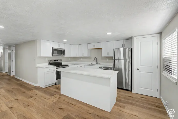 Wood-finish flooring, white cabinetry, stainless steel appliances, white countertops, and a central island with integrated storage