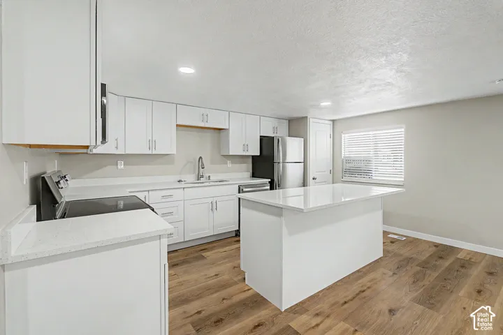 Kitchen featuring white cabinetry, light-toned countertops, a central island, stainless steel appliances, and wood-finish flooring