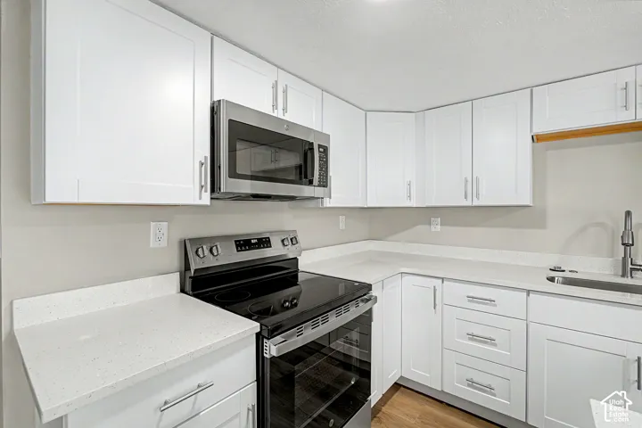 White shaker cabinetry, light-toned countertops, stainless steel appliances, and wood-finish flooring