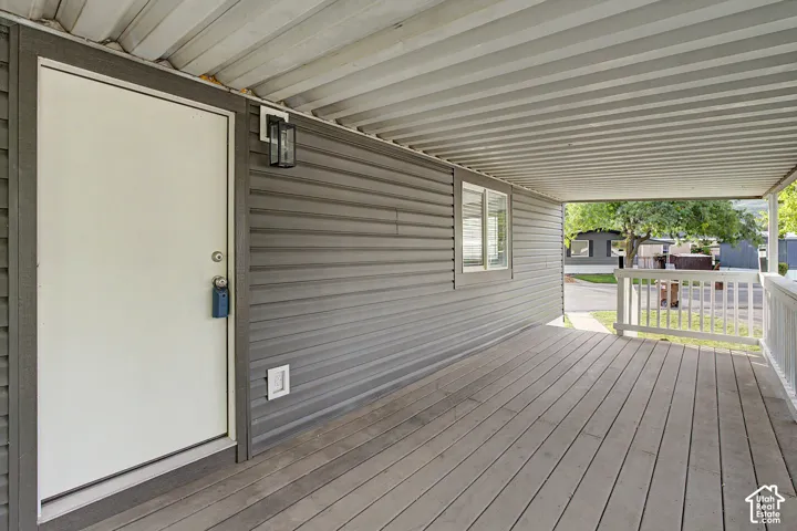Covered porch featuring wood-finish decking, white railings, and gray horizontal siding