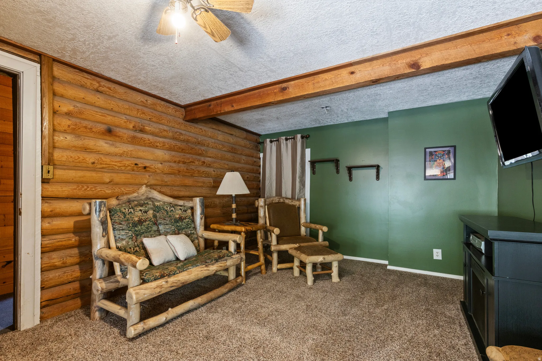 Living area with beamed ceiling, log walls, a textured ceiling, carpet flooring, and ceiling fan