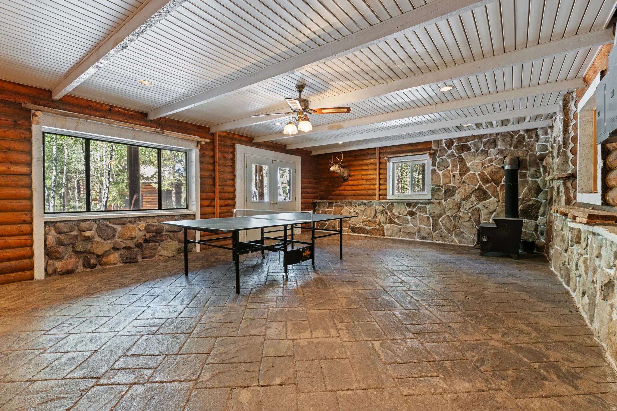 Recreation room with a wood stove, healthy amount of natural light, a ceiling fan, and beamed ceiling