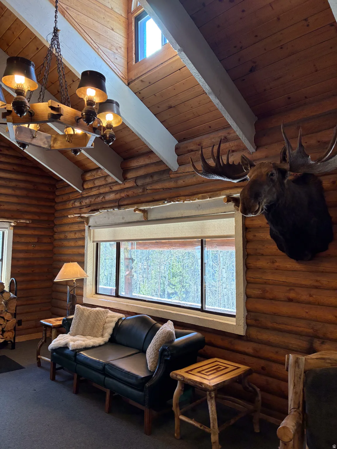 Living room featuring log walls, a wood ceiling with exposed beams, dark carpet, a chandelier, and high vaulted ceiling