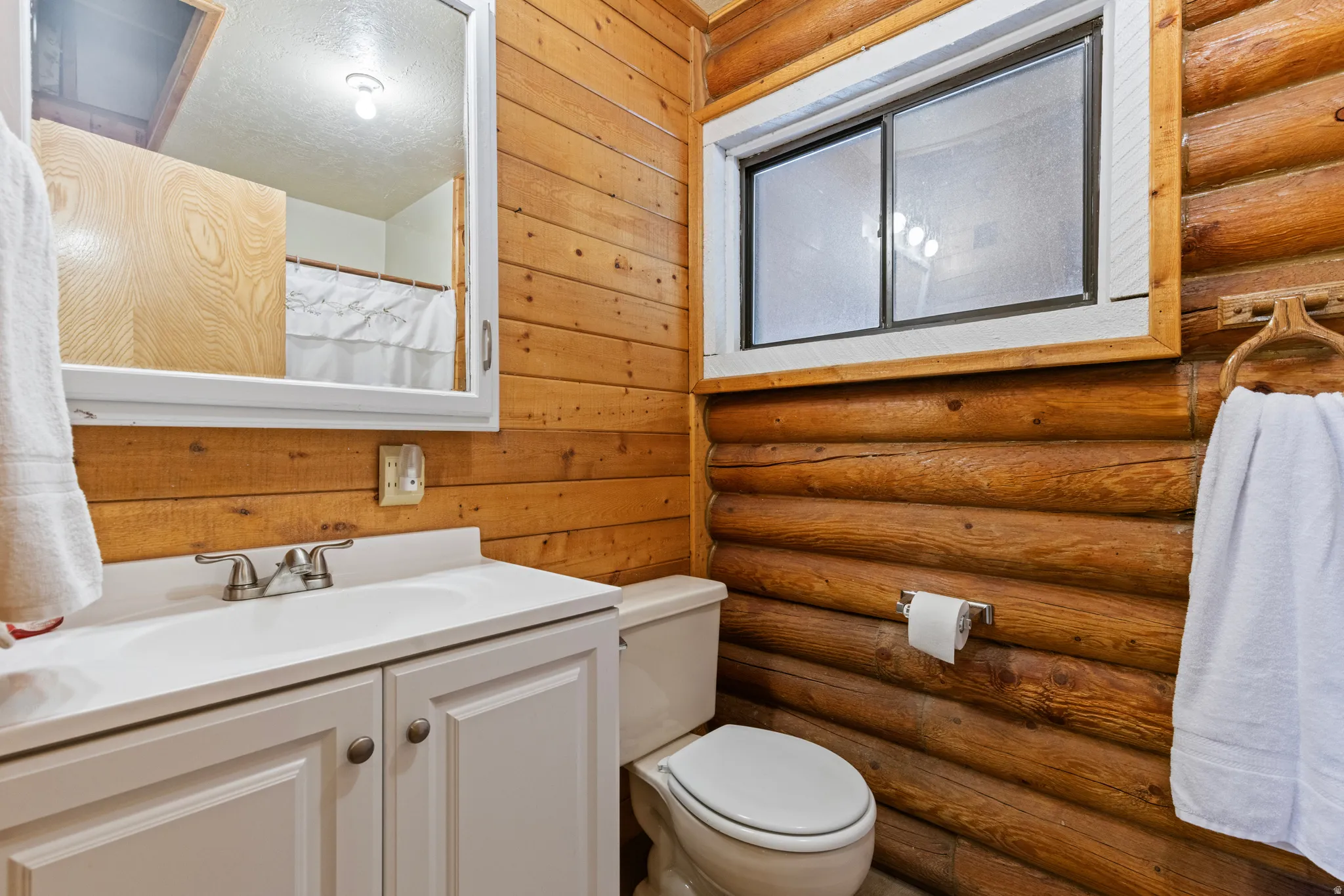 Full bathroom with log walls, a shower with curtain, and vanity