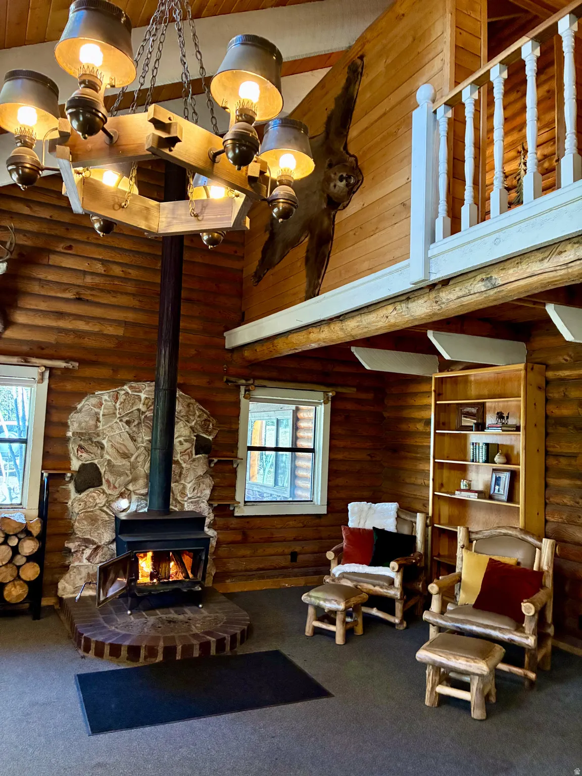 Living area with high vaulted ceiling, a wood stove, rustic walls, carpet flooring, and wood ceiling