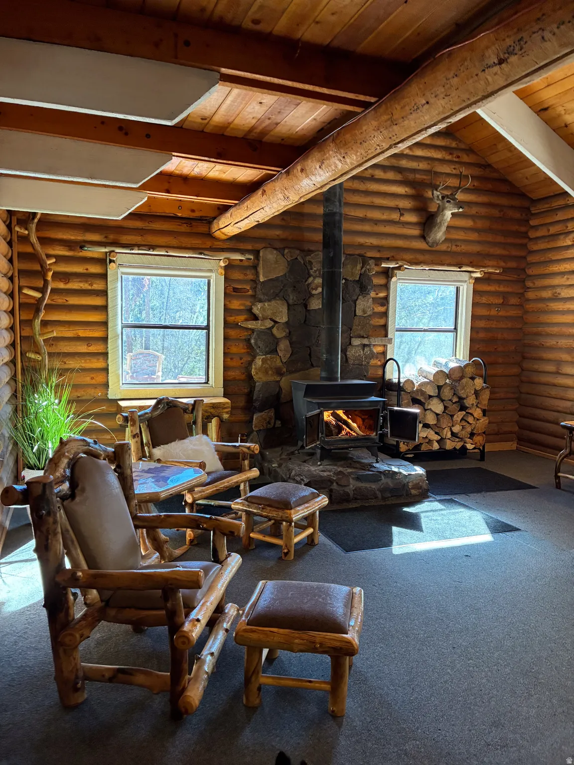 Living area with a wood stove, a wood ceiling with exposed beams, carpet flooring, and rustic walls