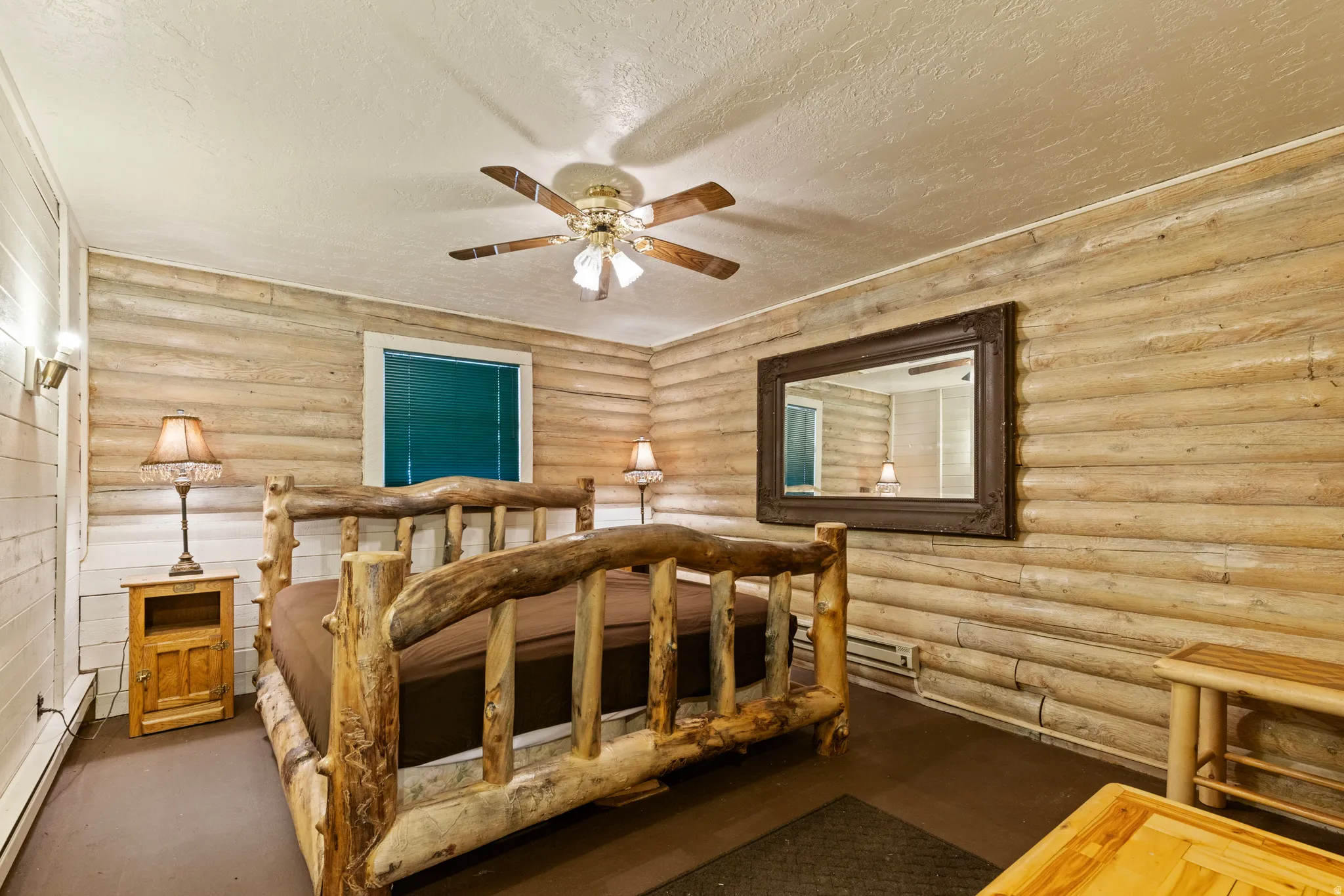 Bedroom featuring a textured ceiling, a baseboard heating unit, a ceiling fan, and rustic walls