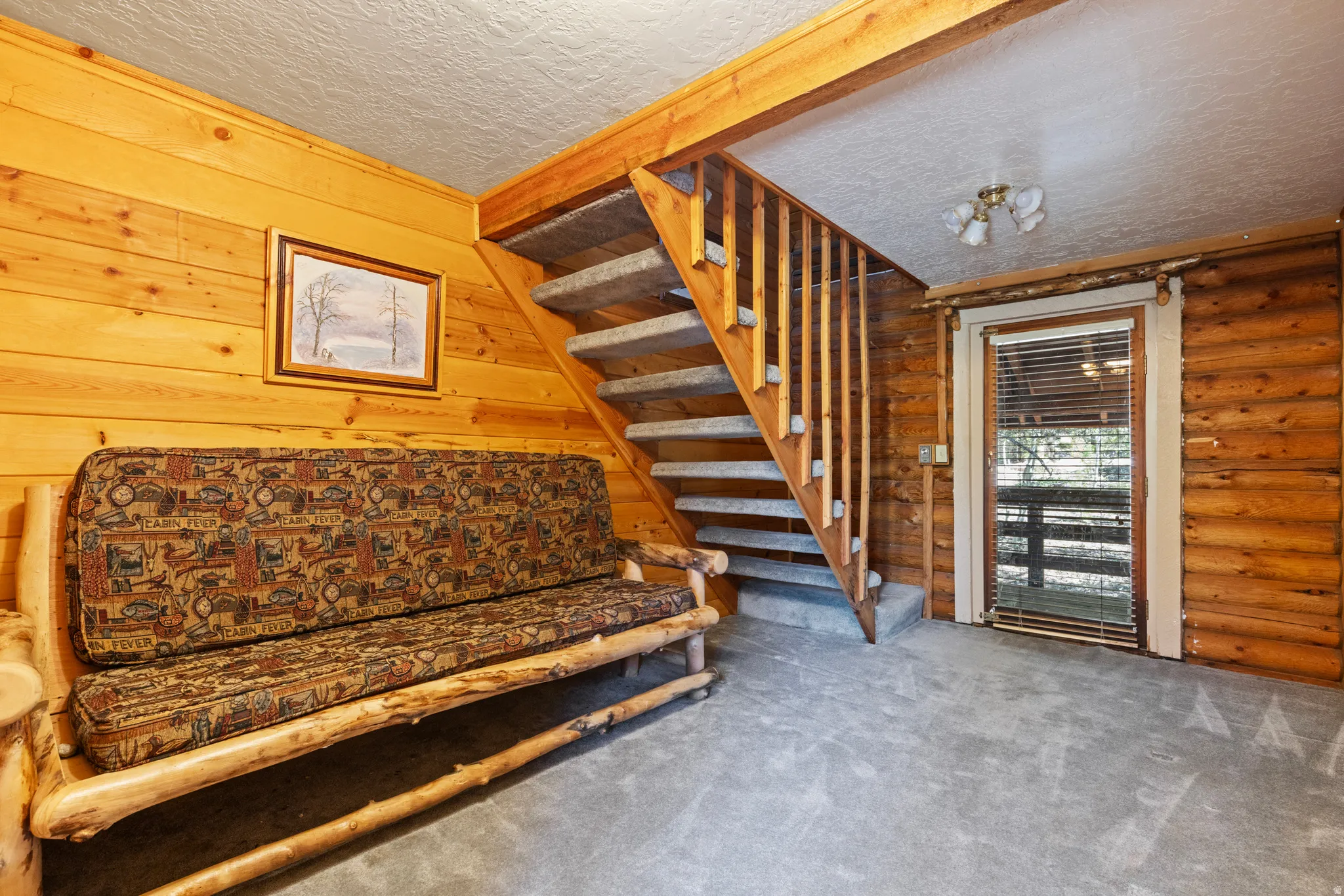 Living area with stairway, wooden walls, carpet flooring, a textured ceiling, and log walls