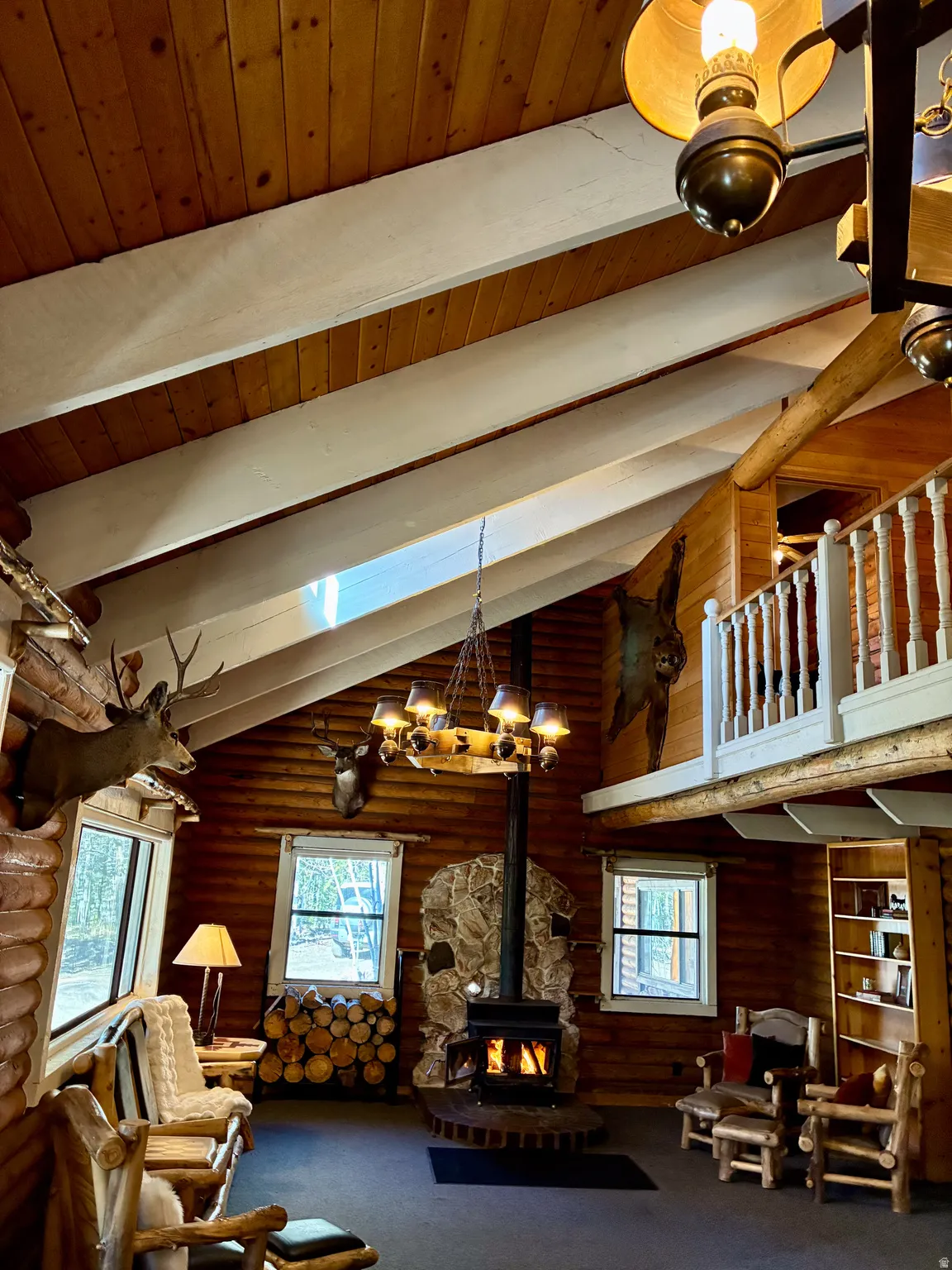Sitting room with a wood stove, a skylight, carpet flooring, a wooden ceiling with exposed beams, and high vaulted ceiling