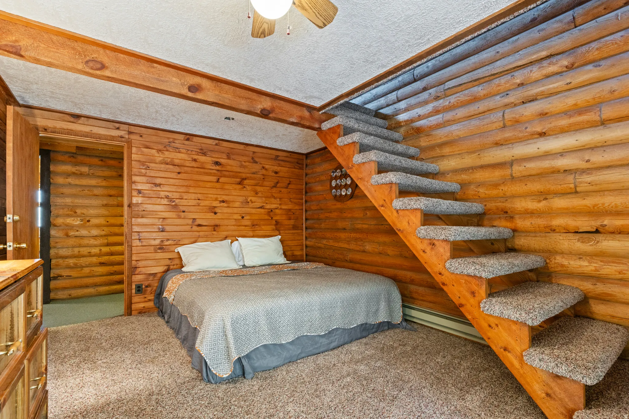 Carpeted bedroom with rustic walls, a textured ceiling, a baseboard radiator, ceiling fan, and beam ceiling