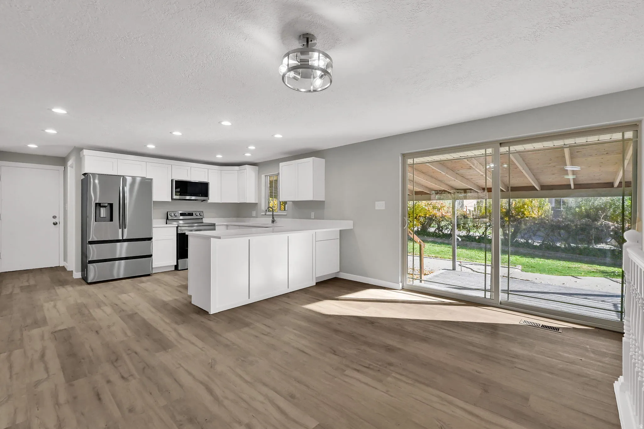 Kitchen with white cabinetry, appliances with stainless steel finishes, recessed lighting, light wood-style floors, and a peninsula