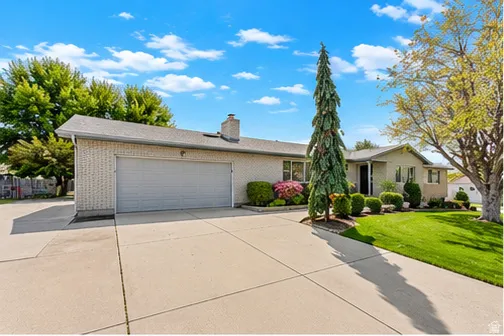 Brick exterior with an attached garage, paved driveway, and manicured landscaping