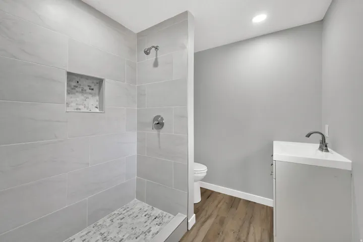 Bathroom with vanity, tiled shower, wood finished floors, and recessed lighting