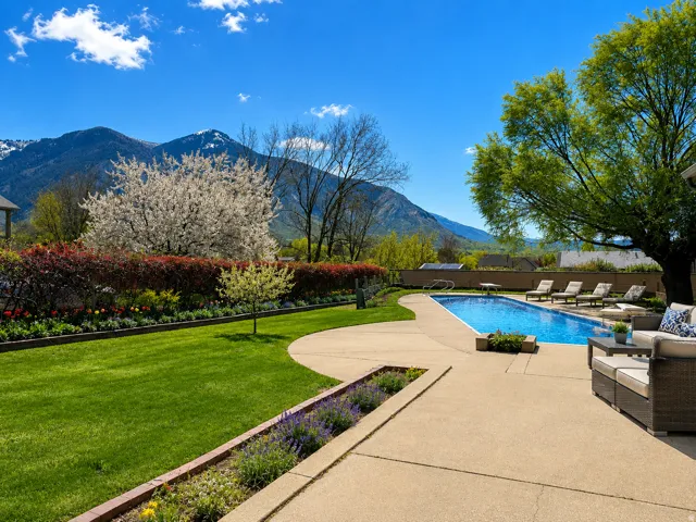 Expansive outdoor space featuring a swimming pool, concrete patio, a manicured lawn, and lush landscaping with mature trees