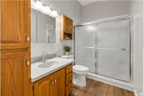 Wood-finish flooring, wood cabinetry with white decorative hardware, white countertop with an undermount sink, and a shower with sliding glass doors