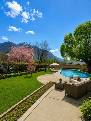 Expansive backyard featuring a curved swimming pool, concrete patio, and manicured lawn