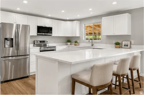 Kitchen featuring white cabinetry, stainless steel appliances, a U-shaped island with a white countertop, recessed lighting, and wood-finish flooring
