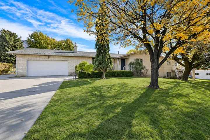 Brick exterior residence featuring a front lawn with mature trees, a multi-car driveway, and an attached garage