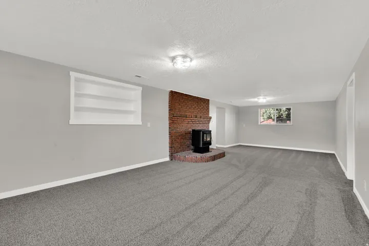 Unfurnished living room featuring built in shelves, carpet floors, a wood stove, and a textured ceiling