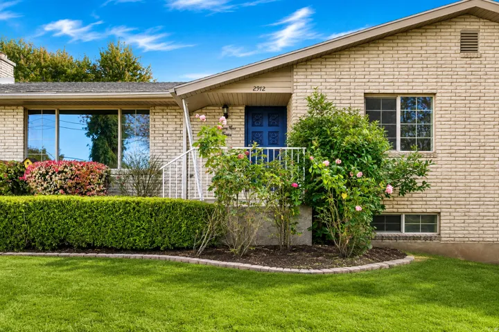 Brick exterior with a prominent blue entry door, an inviting front porch with white railing, and a manicured lawn with mature shrubs