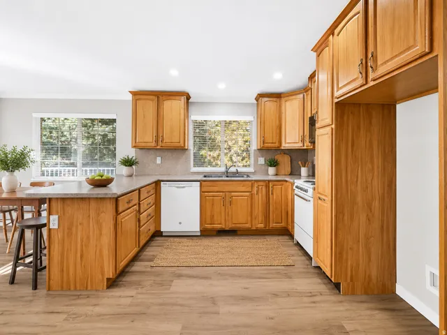 Wood-finish flooring, recessed lighting, wood cabinetry, light-toned countertops, and a white dishwasher