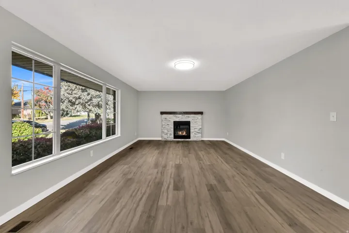 Unfurnished living room with a stone fireplace and dark wood-style flooring