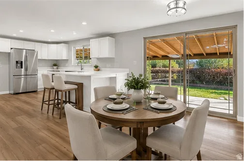 Open-concept kitchen and dining area featuring wood-finish flooring, white cabinetry, stainless steel appliances, and a kitchen island with seating
