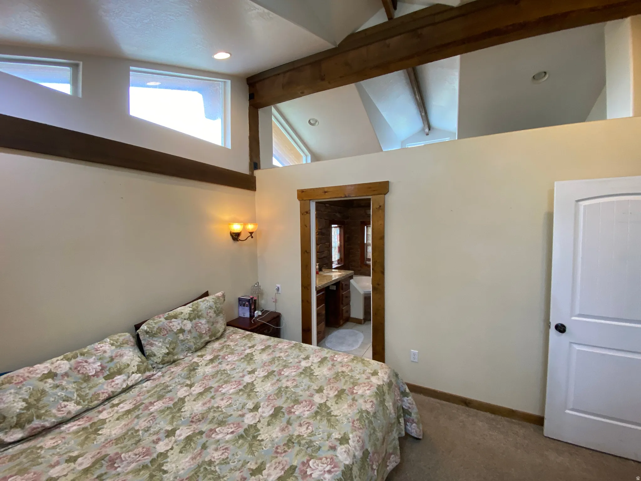 Carpeted bedroom featuring beam ceiling, ensuite bath, and high vaulted ceiling