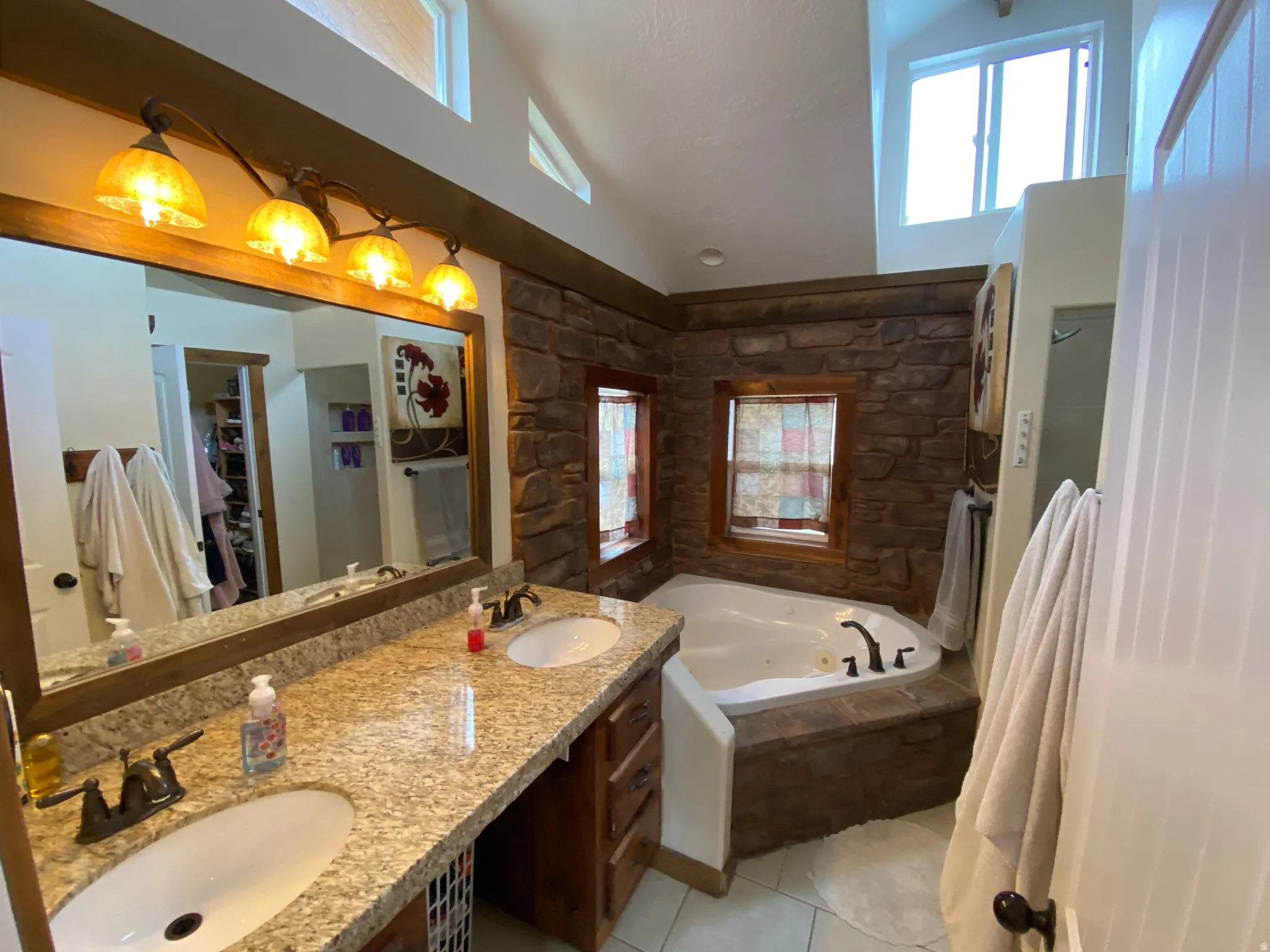 Bathroom featuring double vanity, a whirlpool tub, vaulted ceiling, light tile patterned floors, and a spacious closet