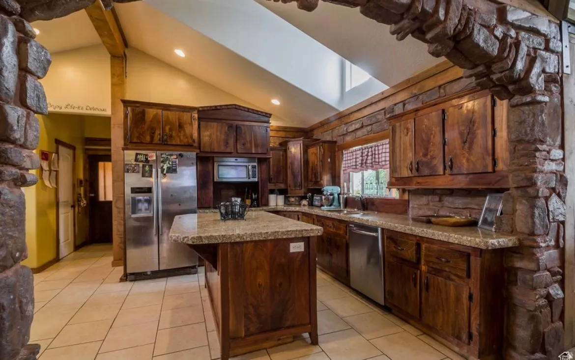 Kitchen with appliances with stainless steel finishes, a center island, dark brown cabinetry, light tile patterned flooring, and high vaulted ceiling