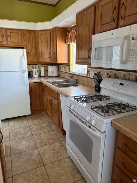 Kitchen with white appliances, brown cabinets, light countertops, ornamental molding, and light tile patterned floors