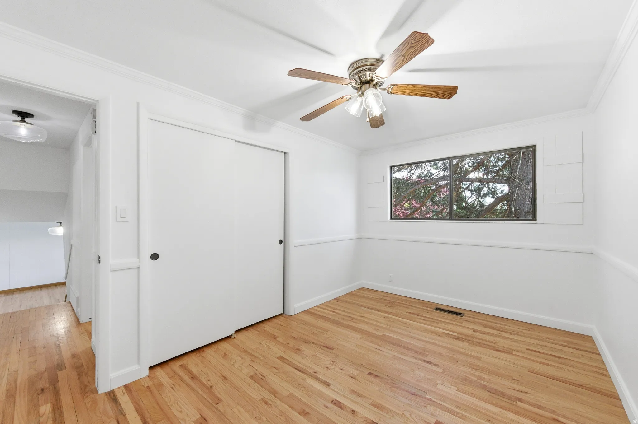 Unfurnished bedroom featuring light wood-style flooring, crown molding, a closet, and ceiling fan