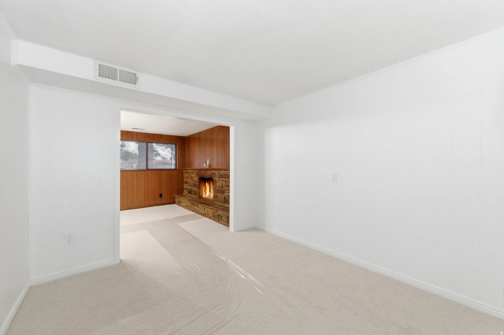 Unfurnished living room with wood walls, a stone fireplace, and light carpet