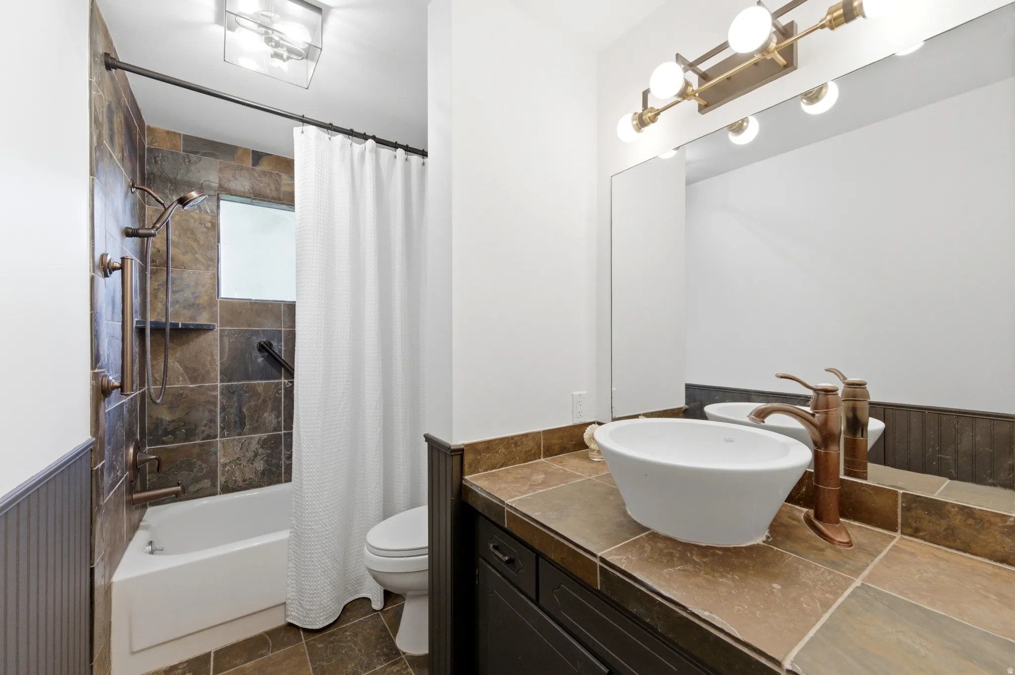 Full bathroom featuring vanity, shower / bath combo, stone tile flooring, and wainscoting