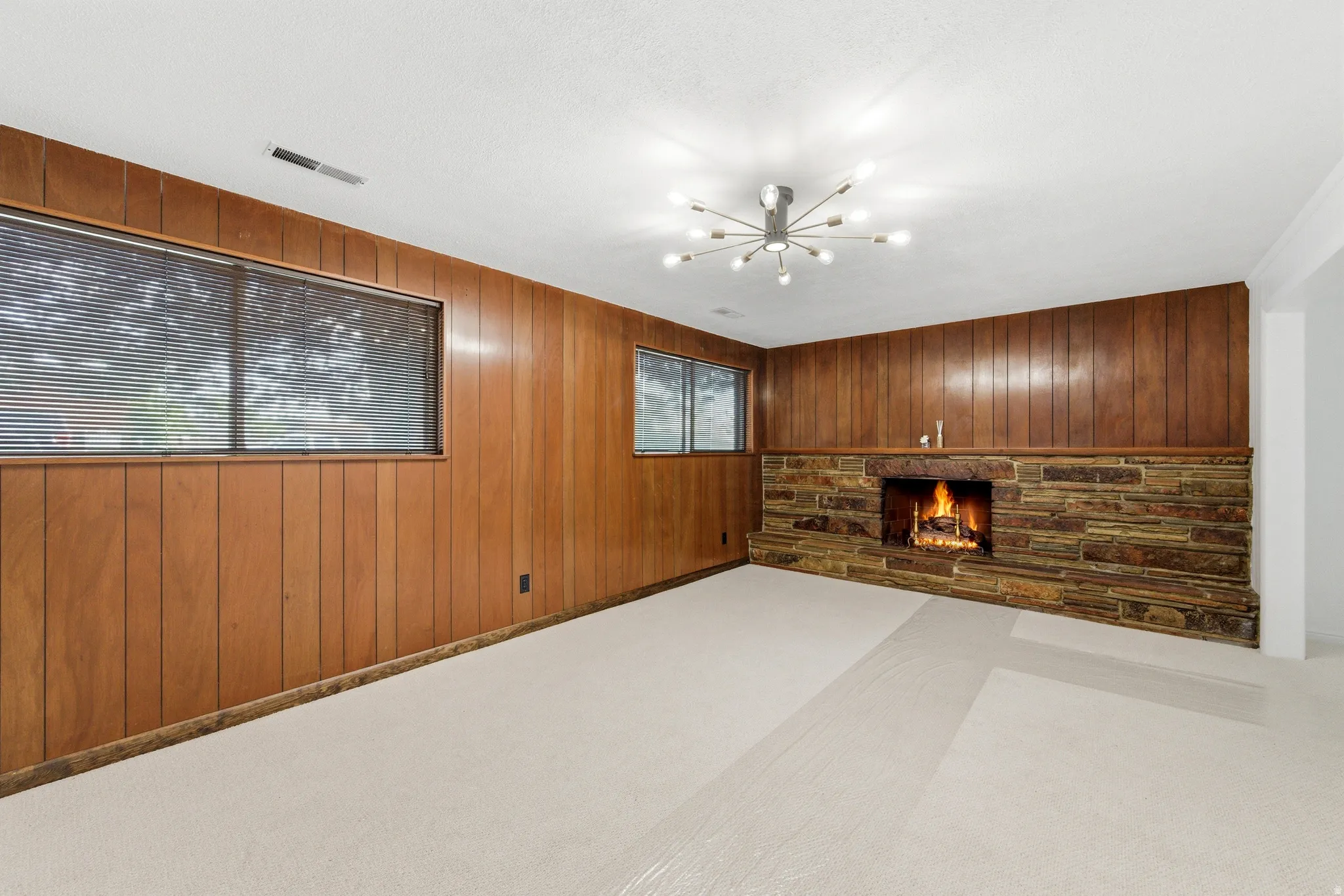 Unfurnished living room featuring wooden walls, a fireplace, carpet, and suspended lighting
