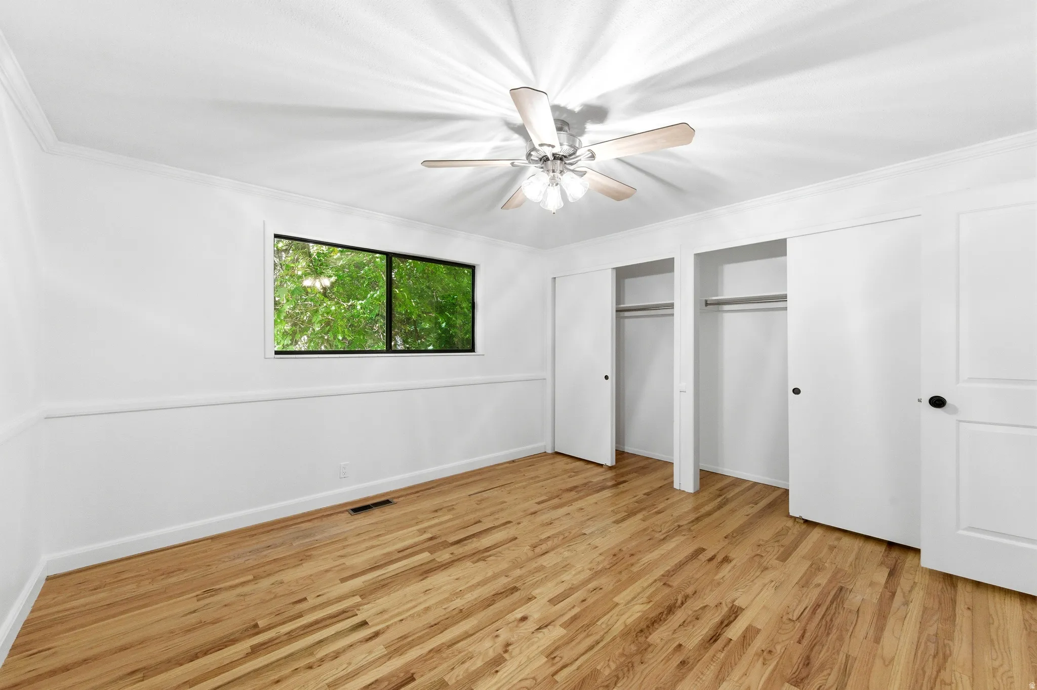 Unfurnished bedroom featuring light wood finished floors, two closets, ornamental molding, and ceiling fan