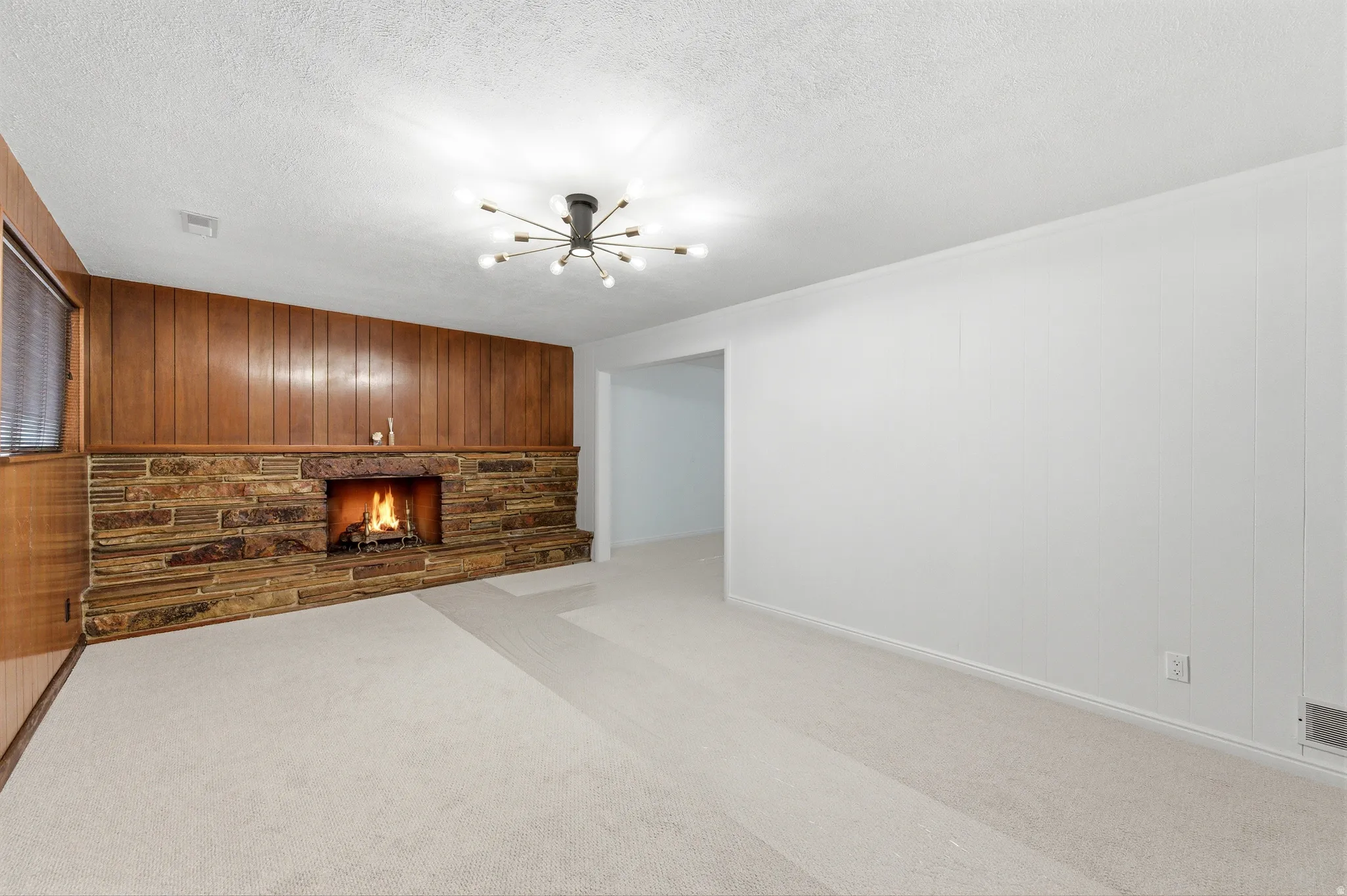 Unfurnished living room with wood walls, carpet, a fireplace, an accent wall, and hanging lights
