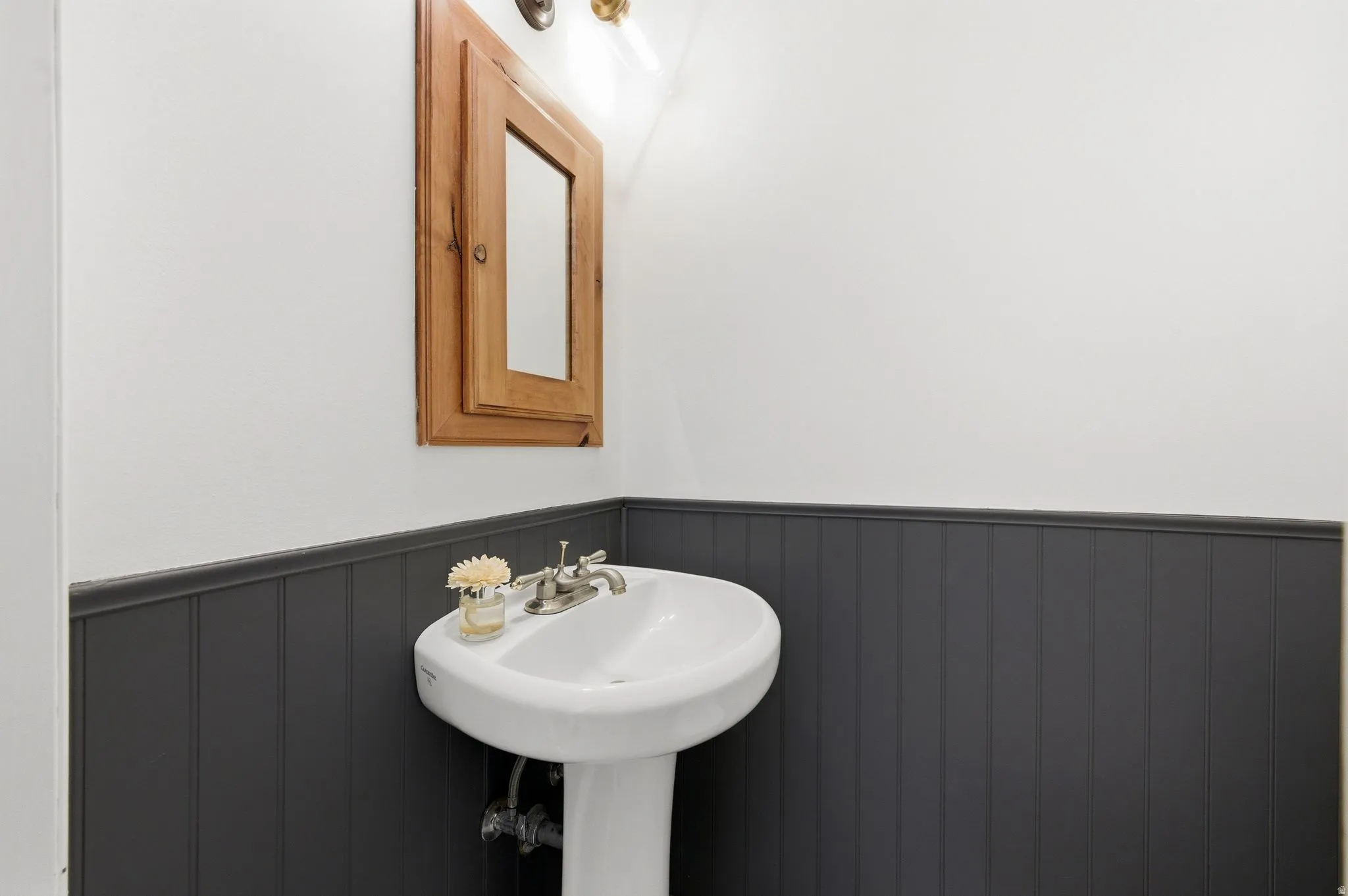 Pedestal sink with brushed nickel faucet, complemented by dark-toned wainscoting