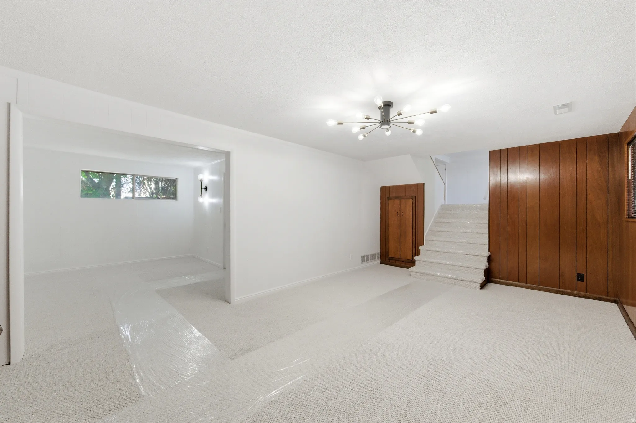 Empty room featuring wood walls, light carpet, and a chandelier