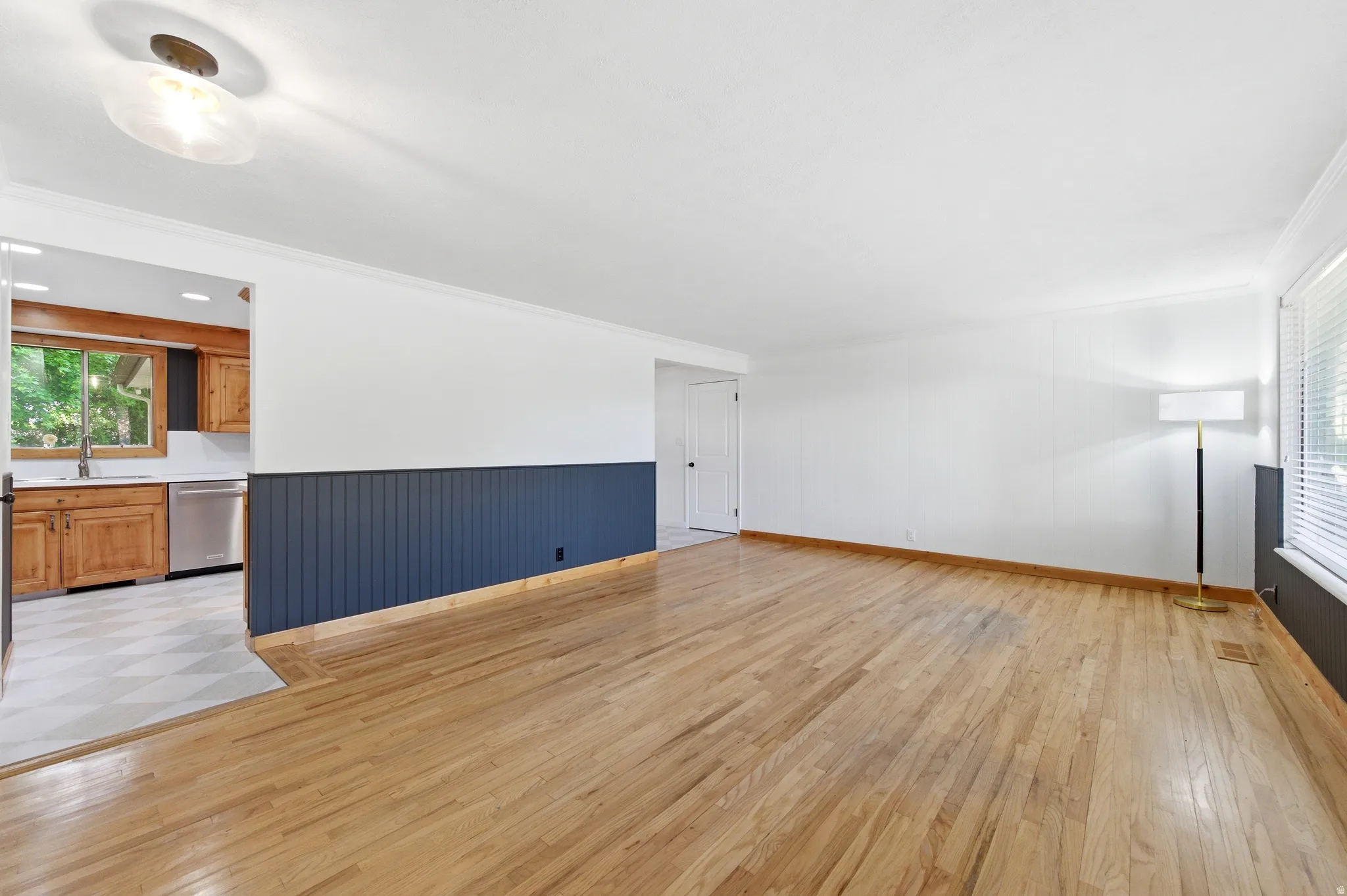 Unfurnished living room featuring crown molding, light wood-type flooring, and wainscoting