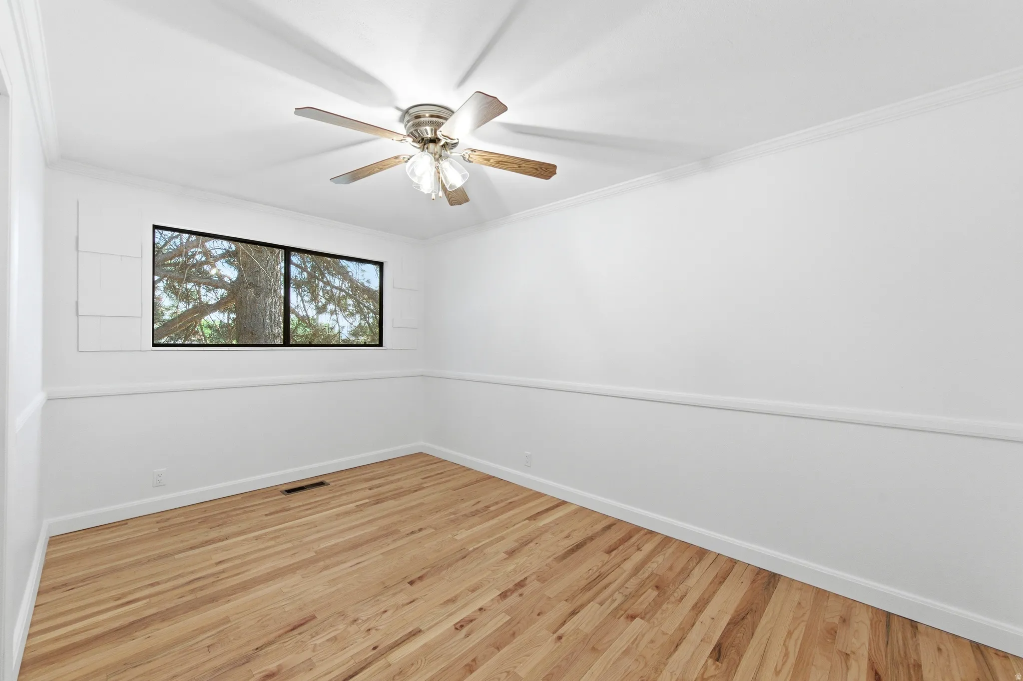 Empty room with ornamental molding, light wood finished floors, and ceiling fan