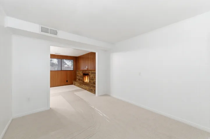 Unfurnished living room with wood walls, a stone fireplace, and light carpet