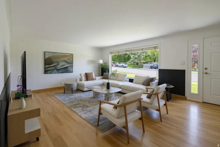 Spacious living area featuring wood-finish flooring, a prominent picture window, and a white paneled accent wall