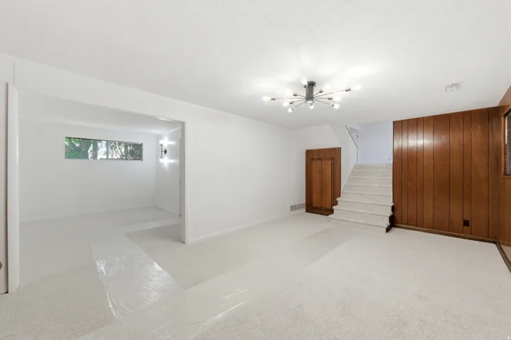 Empty room featuring wood walls, light carpet, and a chandelier