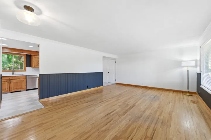 Unfurnished living room featuring crown molding, light wood-type flooring, and wainscoting