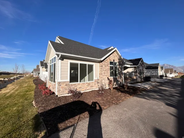 View of property exterior with stone siding, roof with shingles, a lawn, and a residential view