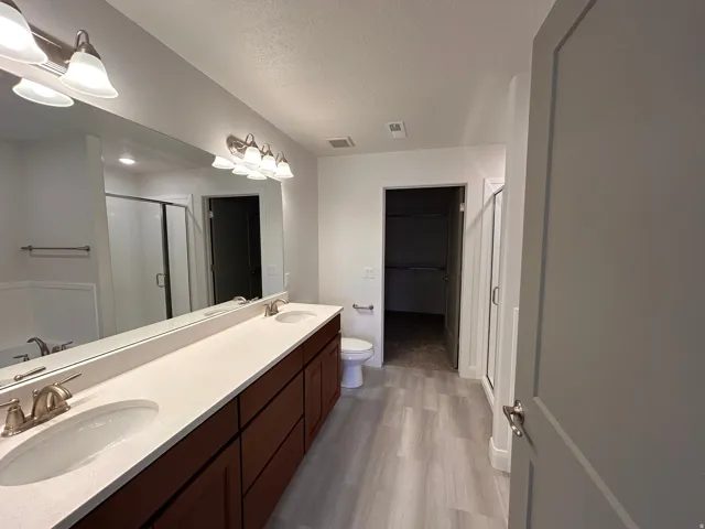 Bathroom with a spacious closet, a stall shower, double vanity, a textured ceiling, and light wood finished floors